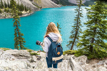 Rückenansicht von Touristen mit Rucksack Schießen auf Kamera malerischen Blick auf Wasseroberfläche und Stein Hügel und bewölkten Himmel in Banff, Kanada - ADSF07414