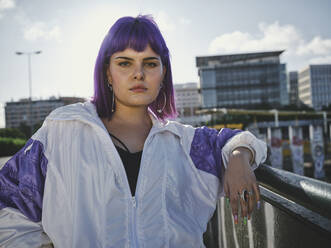 Mode stilvolle Frau mit lila Frisur lehnt auf Metallzaun im Stadtzentrum und selbstbewusst Blick auf die Kamera in hellen Tag - ADSF07453