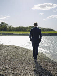 Businessman walking on land at riverbank against sky - GUSF04298