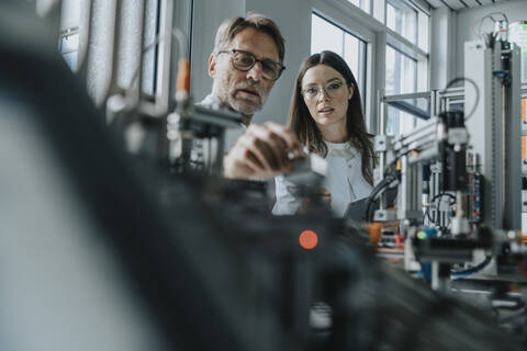 Male scientist with young woman examining machinery in laboratory stock photo