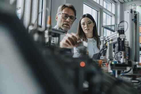 Male scientist with young woman examining machinery in laboratory - MFF05900