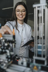 Lächelnde Wissenschaftlerin mit digitalem Tablet bei der Arbeit im Labor einer Fabrik - MFF05910