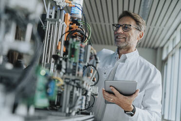 Smiling male scientist holding digital tablet examining machinery in laboratory - MFF05920