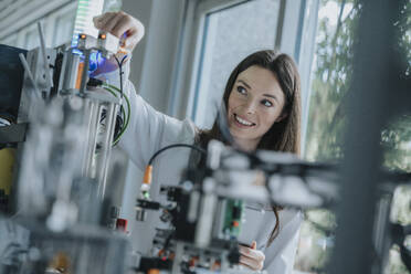 Smiling young woman inventing machinery in laboratory - MFF05928