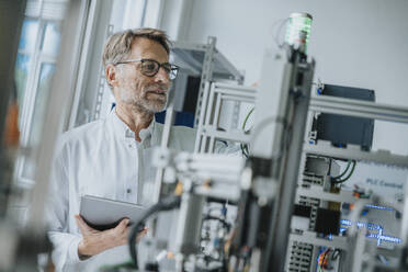 Male scientist wearing eyeglasses with digital tablet looking at machinery in laboratory - MFF05931