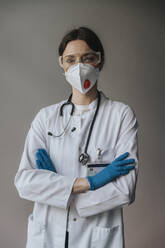 Female doctor wearing mask and protective eyewear with arms crossed standing against wall in hospital - MFF05944