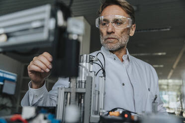 Male scientist with protective eyewear examining machine in laboratory - MFF05945