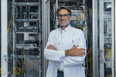 Smiling mature man with arms crossed standing in server room - MFF05962