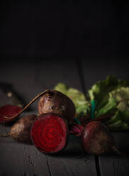 From above dark red sugar beetroots on stem with green leaves on black background - ADSF07645