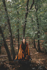 Junge Frau in Schmetterlingsflügeln Umhang tanzen in der Nähe von Bäumen in grünen Wald - ADSF07731