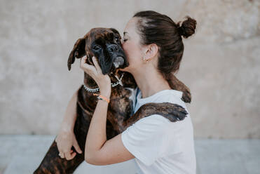 Seitenansicht einer attraktiven Frau und eines Boxerhundes mit freundlichem Gesicht, die sich freuen und umarmen - ADSF07768