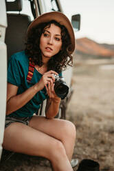 Attraktive junge Frau sitzt in einem coolen Van und hält eine Fotokamera in der Mitte von Nirgendwo im Sommer - ADSF07776