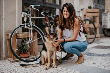 Cute german shepherd standing close bicycle on cobblestone pavement with owner cuddling - ADSF07780