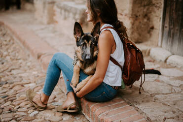 Casual young women sitting on concrete pavement with adorable german shepherd - ADSF07782