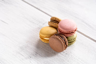 Colorful tasty macaroons stacked in pile against wooden white surface - ADSF07807