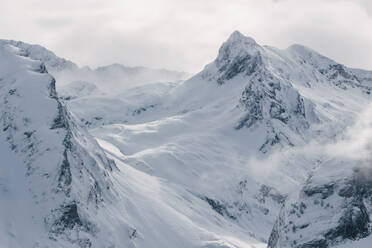 Streng kalte Winterlandschaft mit verschneiten felsigen Berggipfeln und Sonnenlicht, das durch Nebel und Schneesturm bricht - ADSF07810