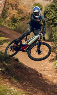 Unbekannter Mann mit Helm, Handschuhen und Schutzbrille beim Peitschentrick bergab während eines Mountainbike-Trainings im Wald - ADSF07815