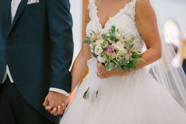 Unkenntlich Ernte Bräutigam in edlen Smoking und Braut in eleganten Hochzeitskleid stehen zusammen während der Zeremonie - ADSF07840