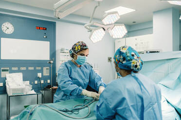 Sanitäter in blauen OP-Kitteln und Schutzmasken bohren Rohre in den Körper eines auf dem Bett liegenden, zugedeckten Patienten - ADSF07959