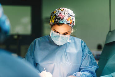 Serious young doctor in protective mask and cap making surgery with instruments and crop nurse - ADSF07965