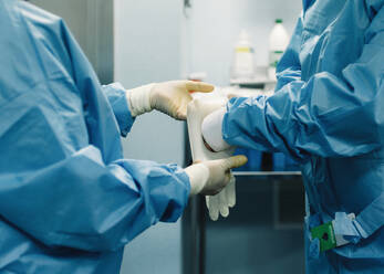 Seitenansicht eines chirurgischen Teams in blauem Kittel, das weiße Handschuhe anzieht und sich auf die Operation vorbereitet - ADSF07969