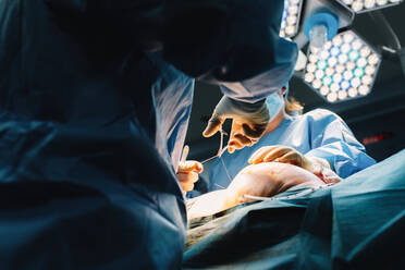 From below plastic surgeon sewing up breast of female patient after inserting implants in operating room - ADSF07974