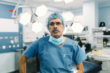 Erwachsener Mann in medizinischer Uniform steht in einem modernen Operationssaal während der Arbeit im Krankenhaus - ADSF07977