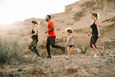 Seitenansicht fröhliche gemischtrassige Familie in sportlicher Kleidung beim Joggen in der Wüstenlandschaft am Morgen - ADSF08028