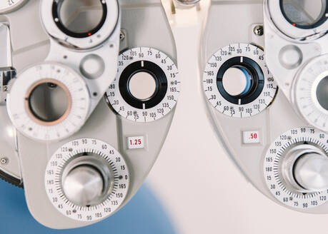 Moderne Sehtestgeräte und ein Stuhl an einer weißen Wand im Büro eines Optikers in einer Klinik - ADSF08044