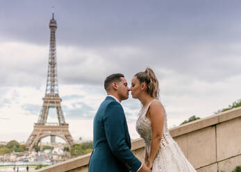 Bräutigam im blauen Anzug und Braut im weißen Hochzeitskleid küssen sich leidenschaftlich mit Eiffelturm im Hintergrund in Paris - ADSF08050