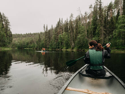 Rückenansicht einer jungen Frau beim Bootfahren auf einem Waldfluss in Finnland - ADSF08066