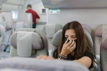 Junge Frau mit geschlossenen Augen und einer Maske, die das Gesicht bedeckt, auf einem Sitz in einem Flugzeug - ADSF08100