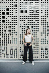 Woman standing against wall with holes in city - MEUF01692