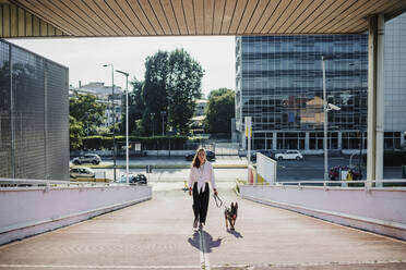 Frau geht mit Hund auf erhöhtem Gehweg spazieren - MEUF01701