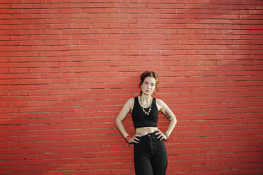 Frau stehend mit Hand auf der Hüfte gegen rote Backsteinmauer - MEUF01712