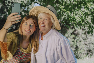 Smiling mid adult woman taking selfie with mother in yard - ERRF04129