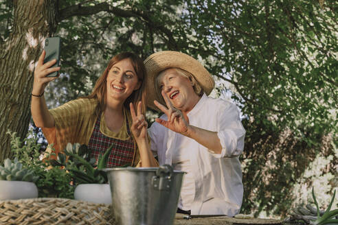 Mid adult woman taking selfie with cheerful mother in yard - ERRF04130