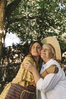 Mother and daughter with eyes closed embracing in yard - ERRF04131