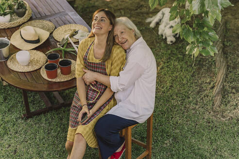 Happy mother embracing daughter while sitting by table in yard - ERRF04132