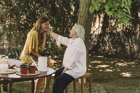 Mother touching daughter's face while sitting in yard - ERRF04133