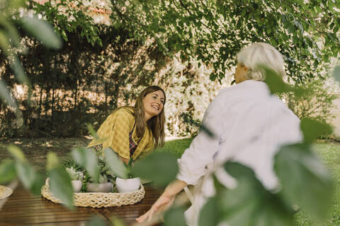 Smiling woman talking with mother while sitting at table in yard stock photo