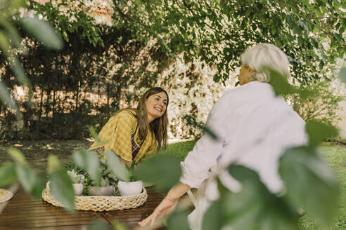 Smiling woman talking with mother while sitting at table in yard - ERRF04147