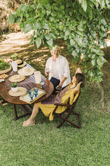 Cheerful mother and daughter enjoying picnic while sitting in yard - ERRF04160