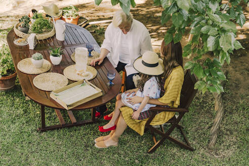 Multi-generation family enjoying picnic at table in yard - ERRF04166