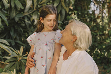 Smiling senior woman looking at cute granddaughter against plants in yard - ERRF04182