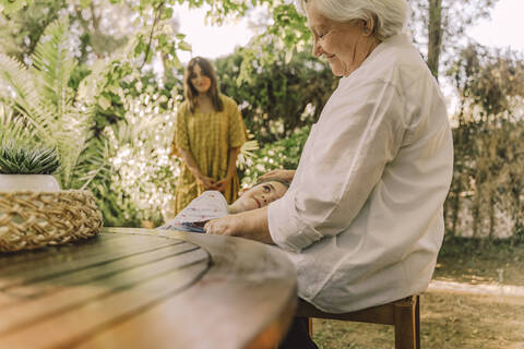 Woman looking at girl lying on grandmother's lap in yard stock photo