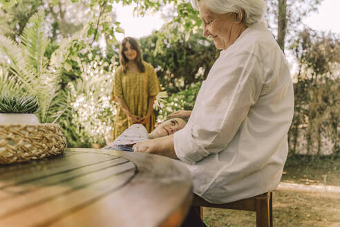 Woman looking at girl lying on grandmother's lap in yard - ERRF04187