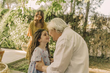 Smiling woman looking at girl playing with grandmother in yard - ERRF04188