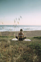 Young woman meditating at beach against clear sky during sunset - MTBF00565