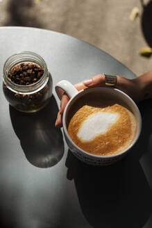 Nahaufnahme einer Frau, die eine Kaffeetasse auf einem Tisch in einem Straßencafé hält - JMPF00266